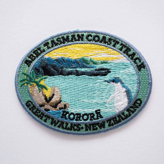 Oval, embroidered Abel Tasman Coast Track patch, with a penguin, blue sea and yellow sky.