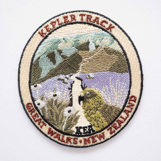 Oval, embroidered Kepler Track patch, with a kea, mountain daisy and alpine ridges.