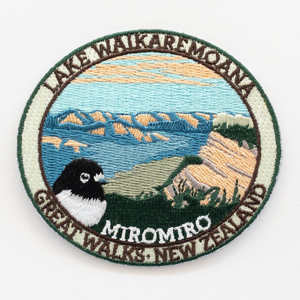Oval, Embroidered Lake Waikaremoana Track patch, with a miromiro/tomtit bird, blue sky, hills and blue lake.