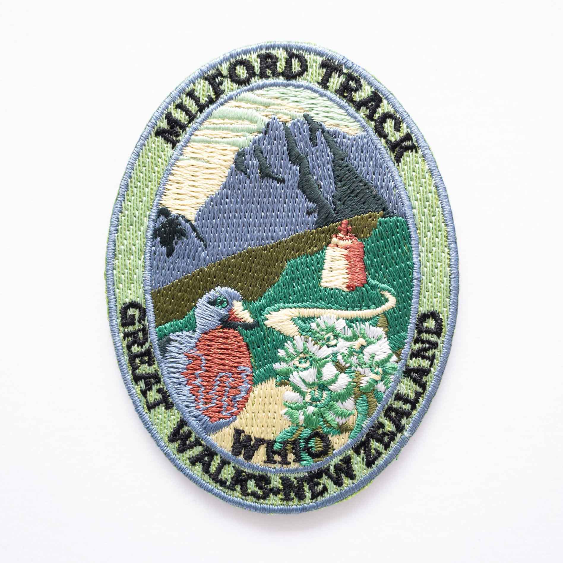 Oval, embroidered Milford Track patch, with a whio/blue duck, blue peak and mountain buttercup.