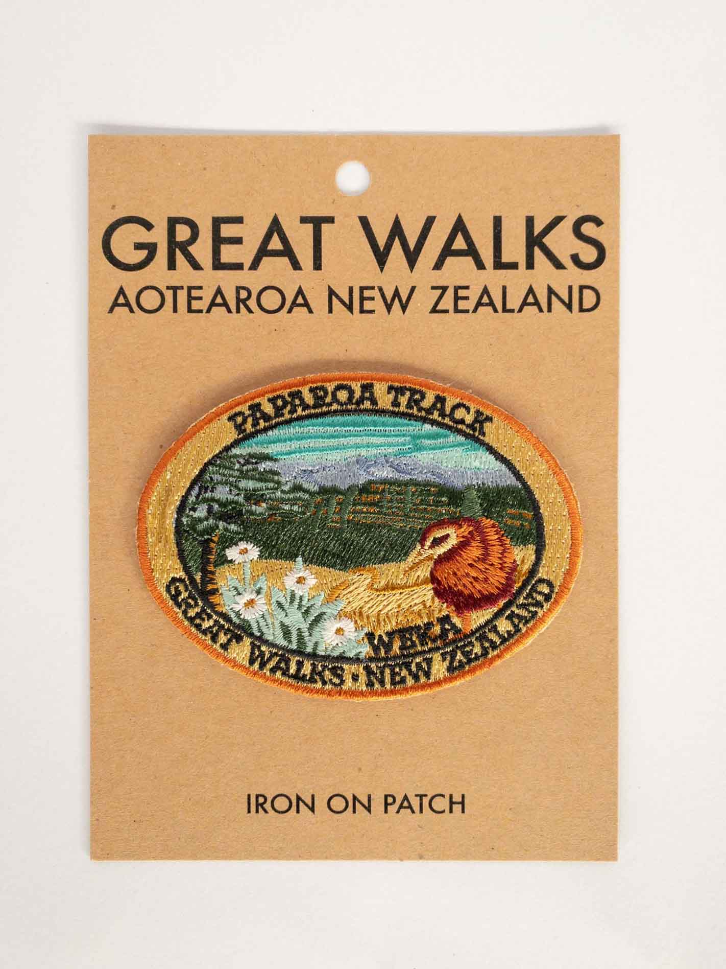 Oval, embroidered Paparoa Track patch, with a weka, green hills, mountain daisy and tussock, on brown kraft backing card.